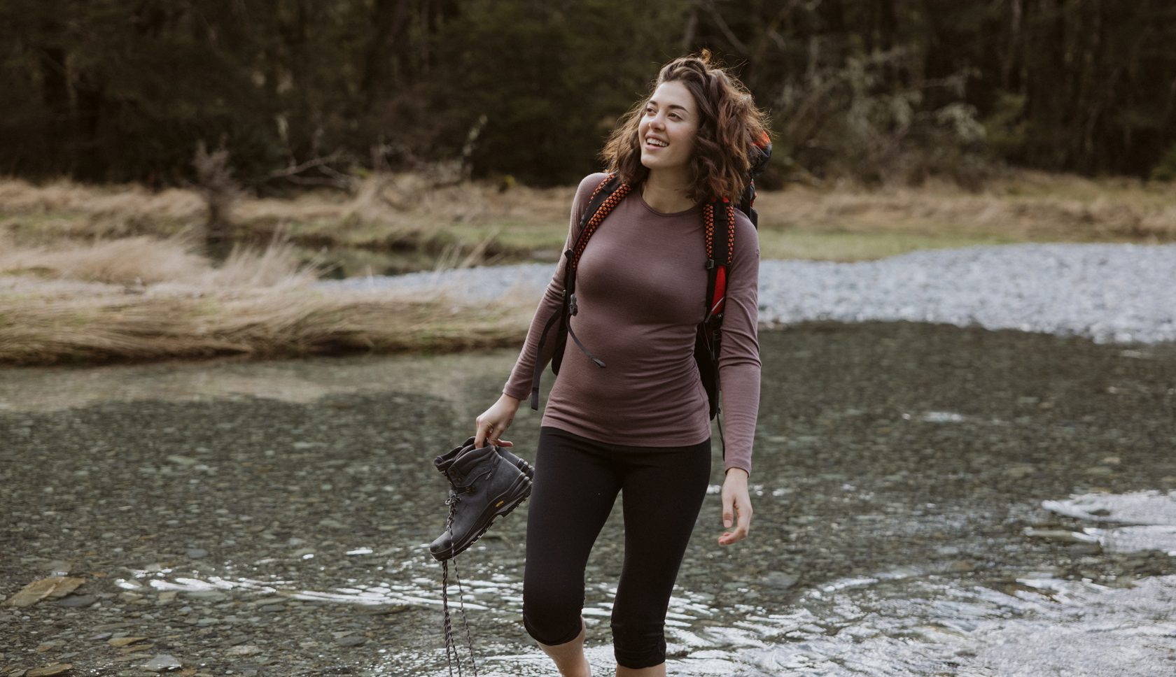vrouw loopt met wandelschoenen in de hand en blote voeten door het water