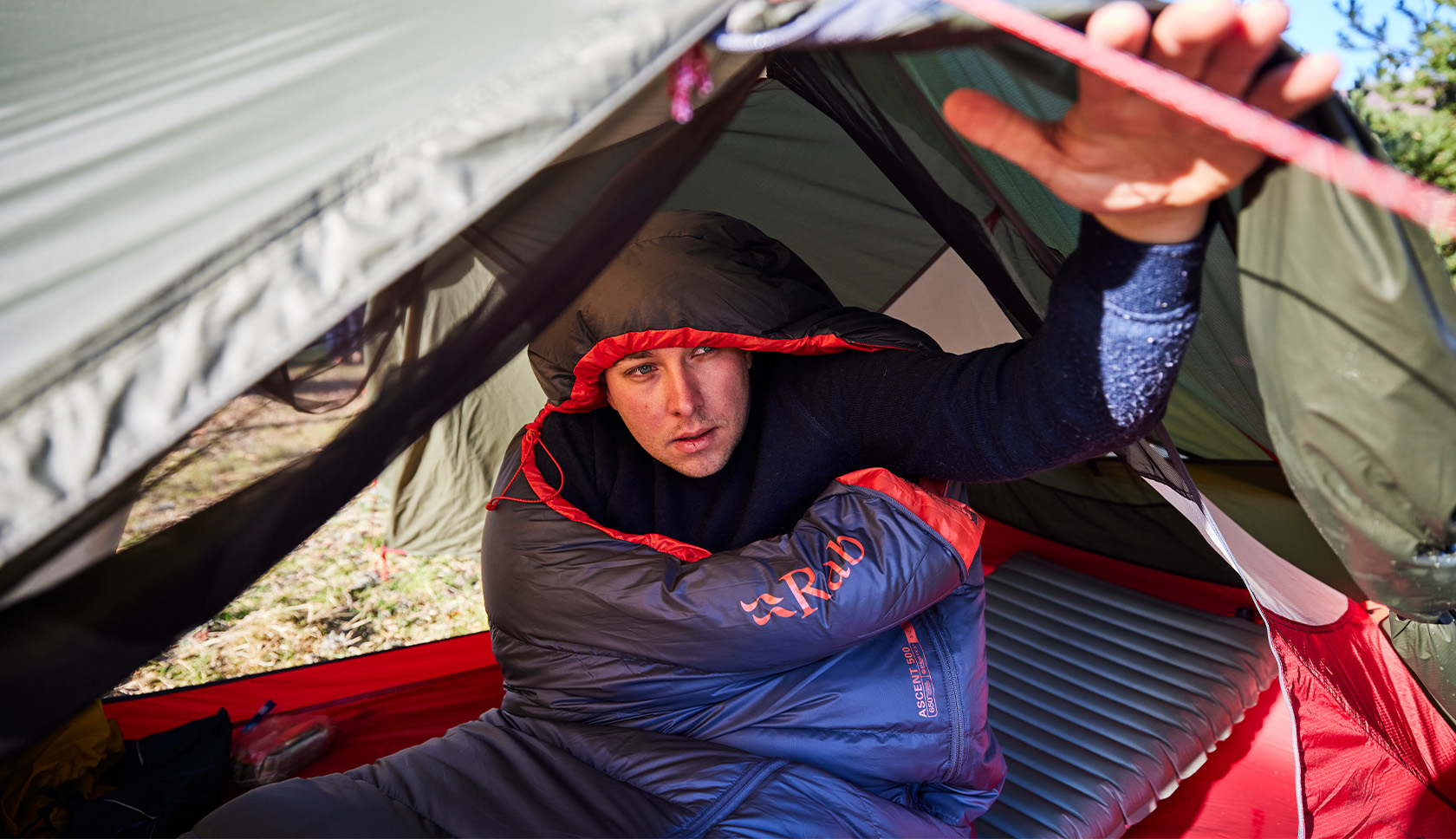 man in slaapzak opent tent