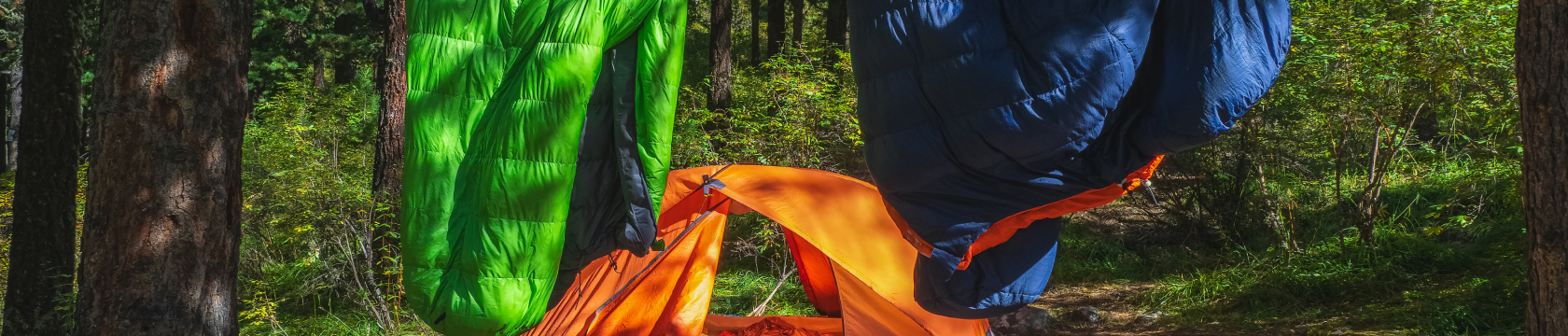 Twee gekleurde slaapzakken hangen over een waslijn in de natuur.