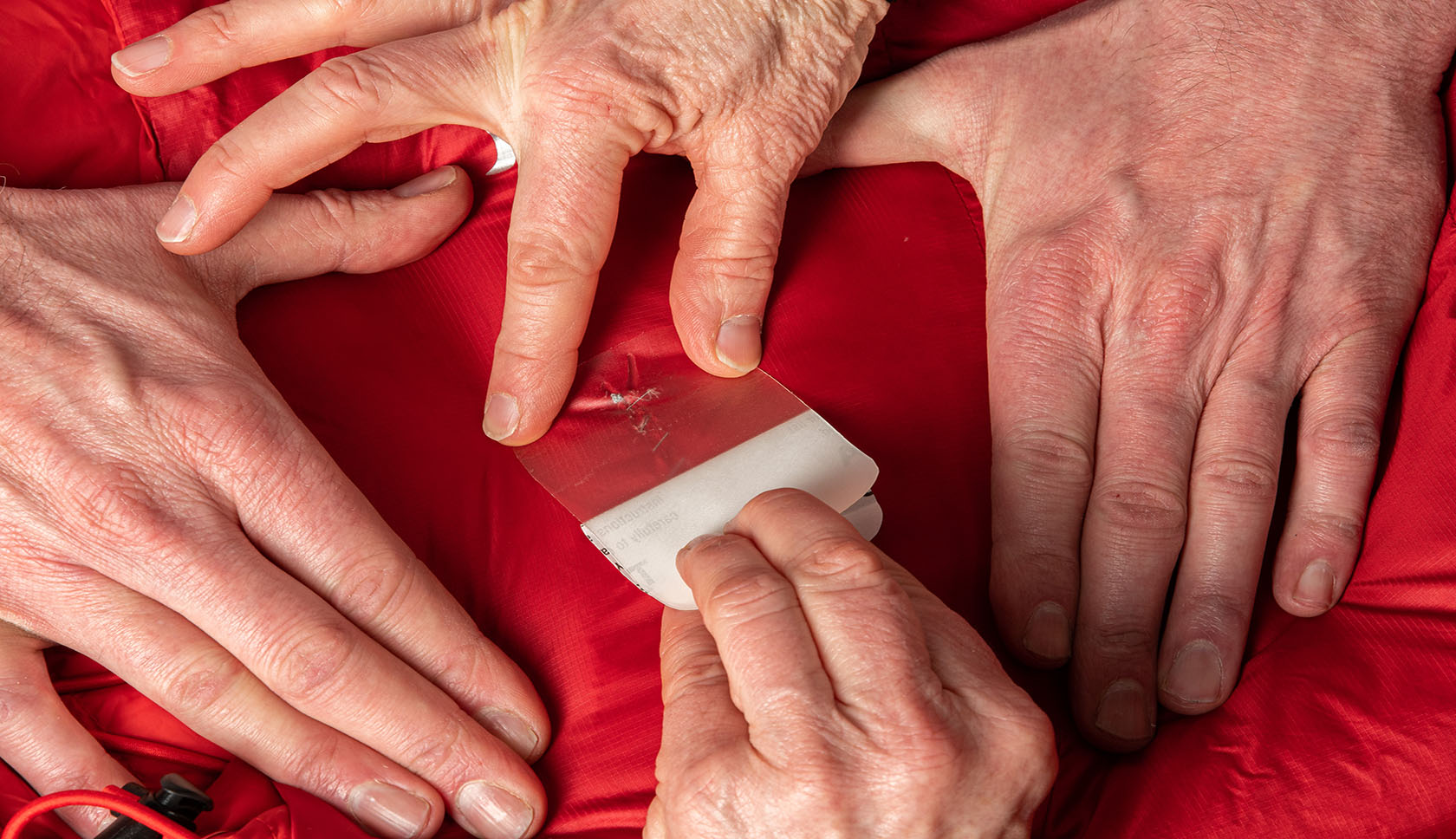 handen plakken een witte patch over een rode donsjas